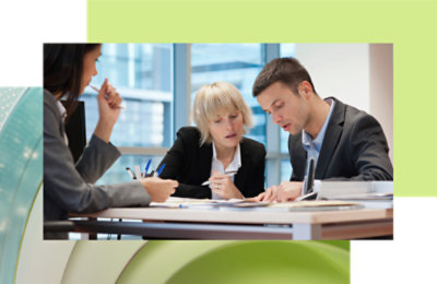 Two professionals, a man and a woman, focused on reviewing document another woman sits beside, listening.