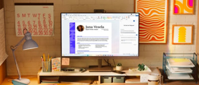 Desktop workspace with a large monitor displaying a professional profile interface, surrounded by office supplies and decorative wall art.