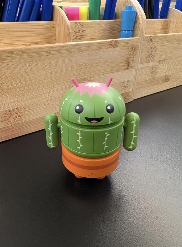 Un petit robot Android vert avec un design en forme de cactus est assis sur une surface noire.
