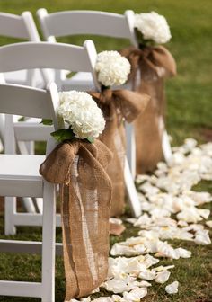two white chairs with burlocks tied to them and some flowers on the ground