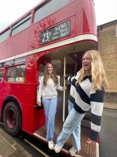 two women standing on the back of a red double decker bus
