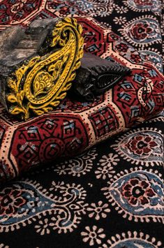 a pile of black and yellow rugs sitting on top of a carpet covered in paisley patterns