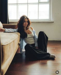 a woman sitting on the floor in front of a window with her legs crossed and looking off to the side