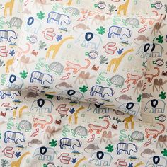 an animal print sheet set on top of a white bedding with blue, green, yellow and red elephants