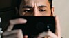 Man looking at a smartphone in dim light, close-up indoor shot.