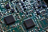 Close-up of a printed circuit board with several black integrated circuits and fine copper traces.