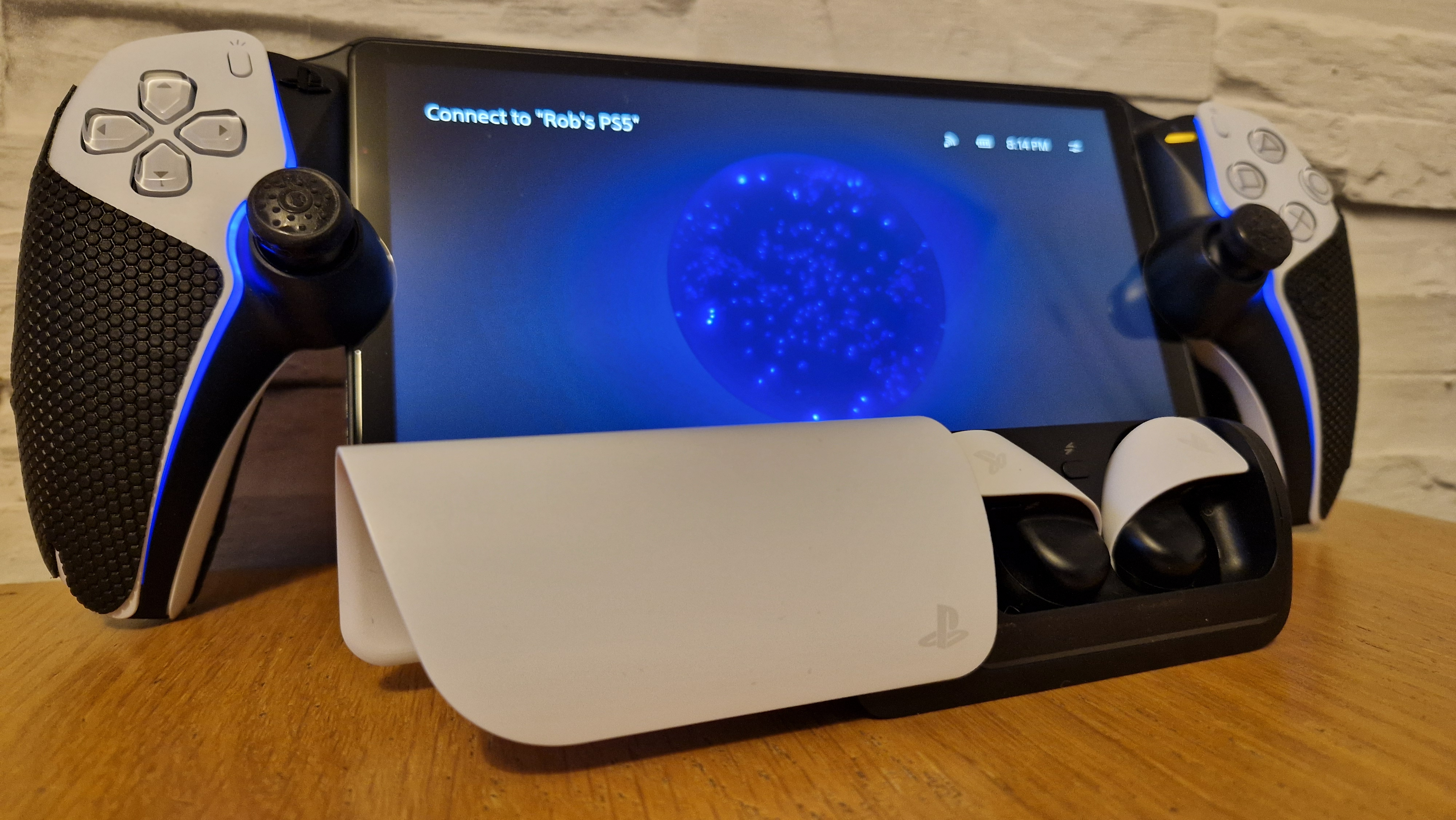 PlayStation Pulse Explore earbuds on a wooden surface with a white brick background