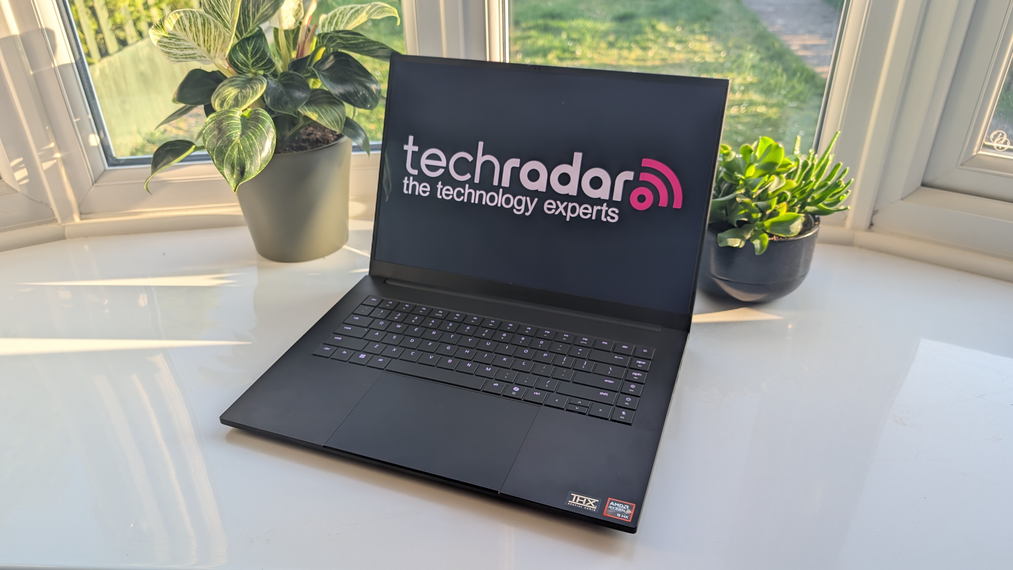 The Razer Blade 16 photographed for TechRadar on a white surface with plants in the background.