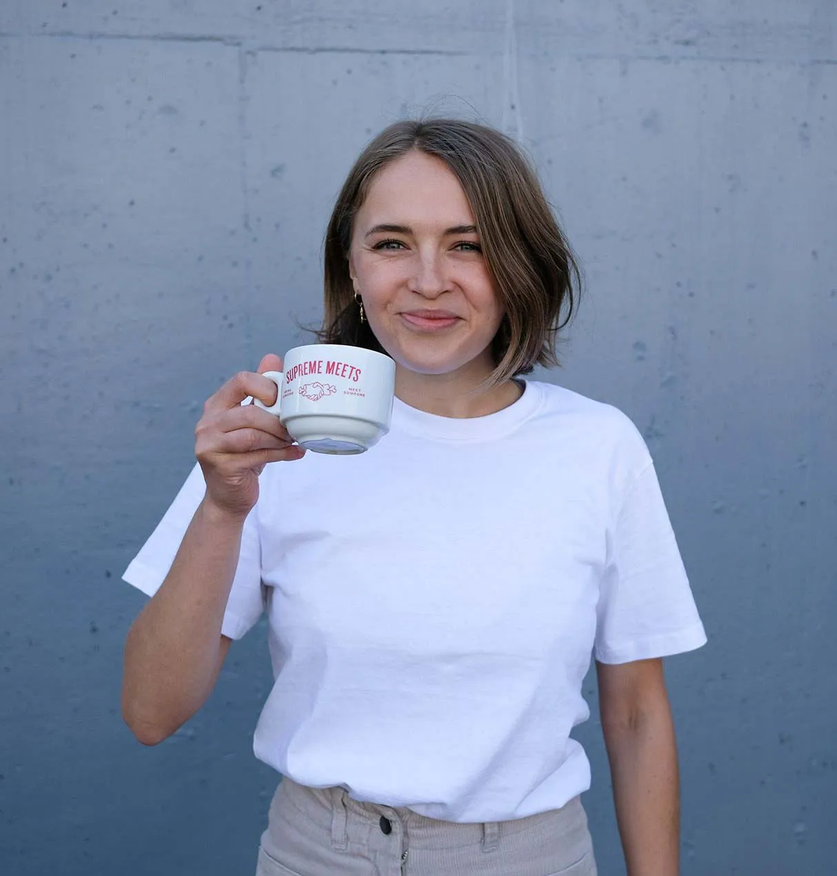 A woman drinking a coffee with the logo Coffee Supreme.