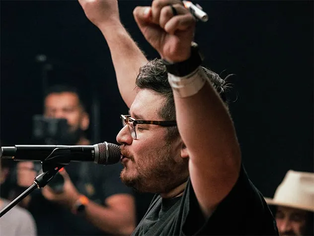 A worship leader singing on a microphone with his eyes closed and his hands raised.