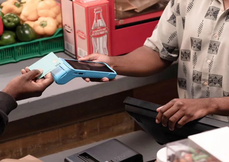 Customer tapping a credit card on a handheld payment terminal held by a cashier at a market.
