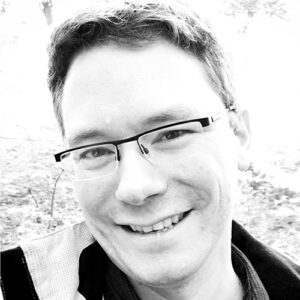 Photo of Nicolai Marquardt who is Co-Chair for Courses at CHI 2022. Nicolai is wearing glasses and is smiling at the camera. The photo is black & white.