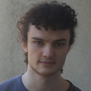 Ciabhan Connelly is looking into the camera and smiling. He is in front of a plain background.