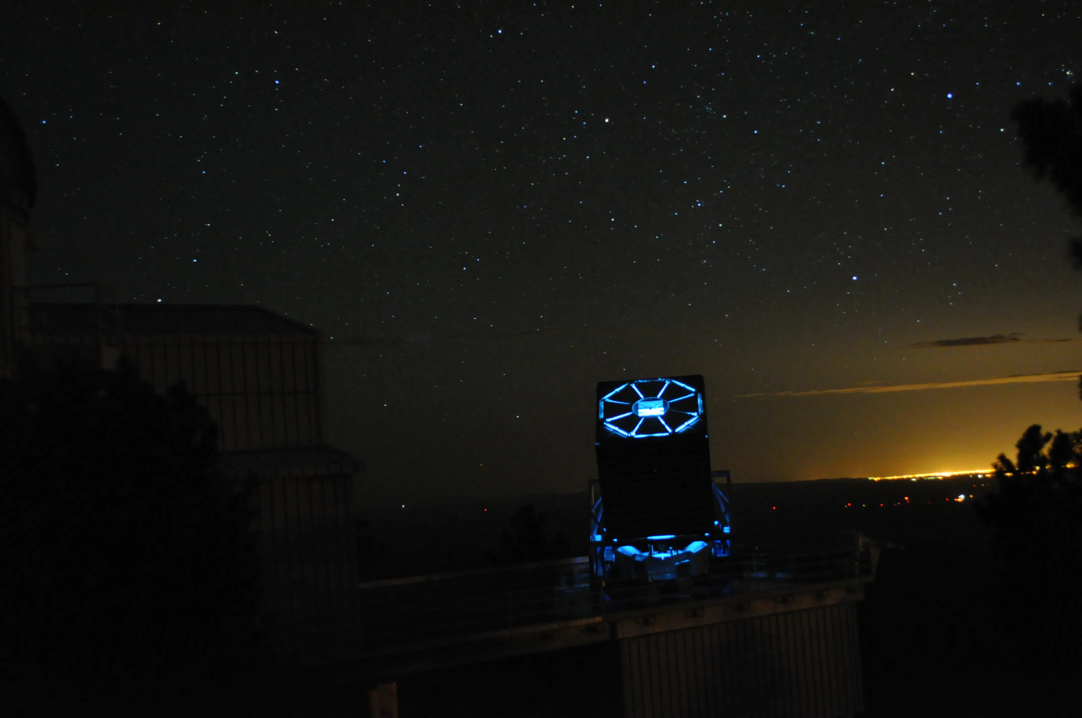 Below a starry sky, the SDSS telescope sits with its shutters closed. It is illuminated internally by a blue ligh