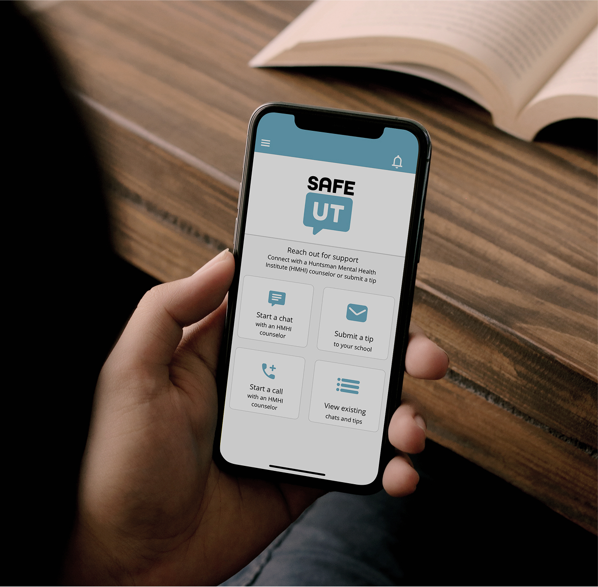 Person holding a smartphone displaying the SafeUT app interface.