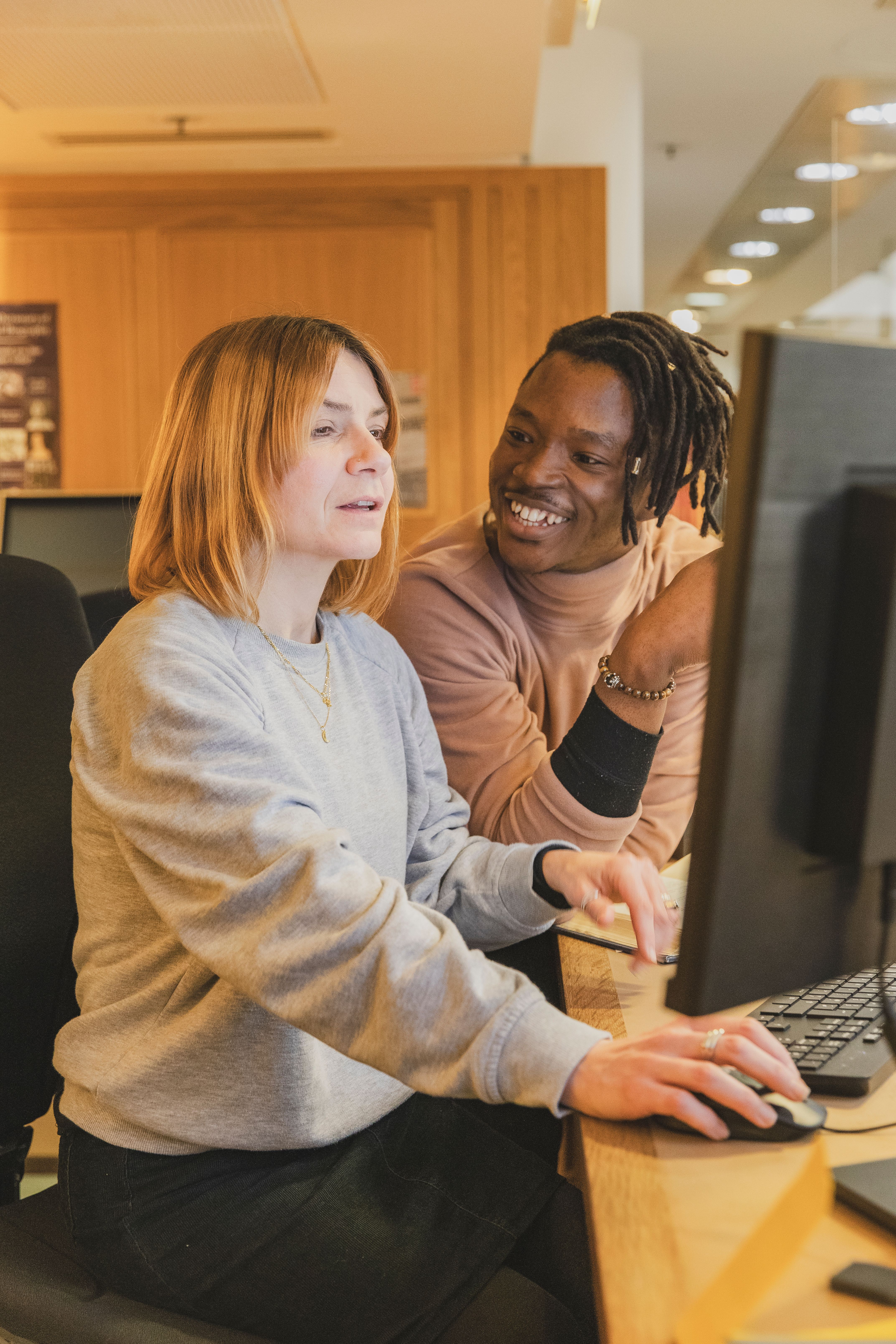 A young man talks to a woman in front of a computer screen at the Reading Room helpdesk in the British Library in London