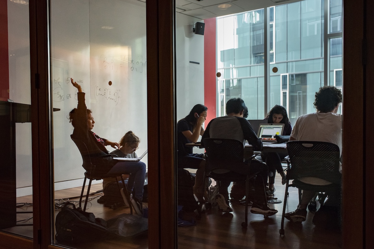 A woman in a conference room raises her hand, as seen through the class walls.