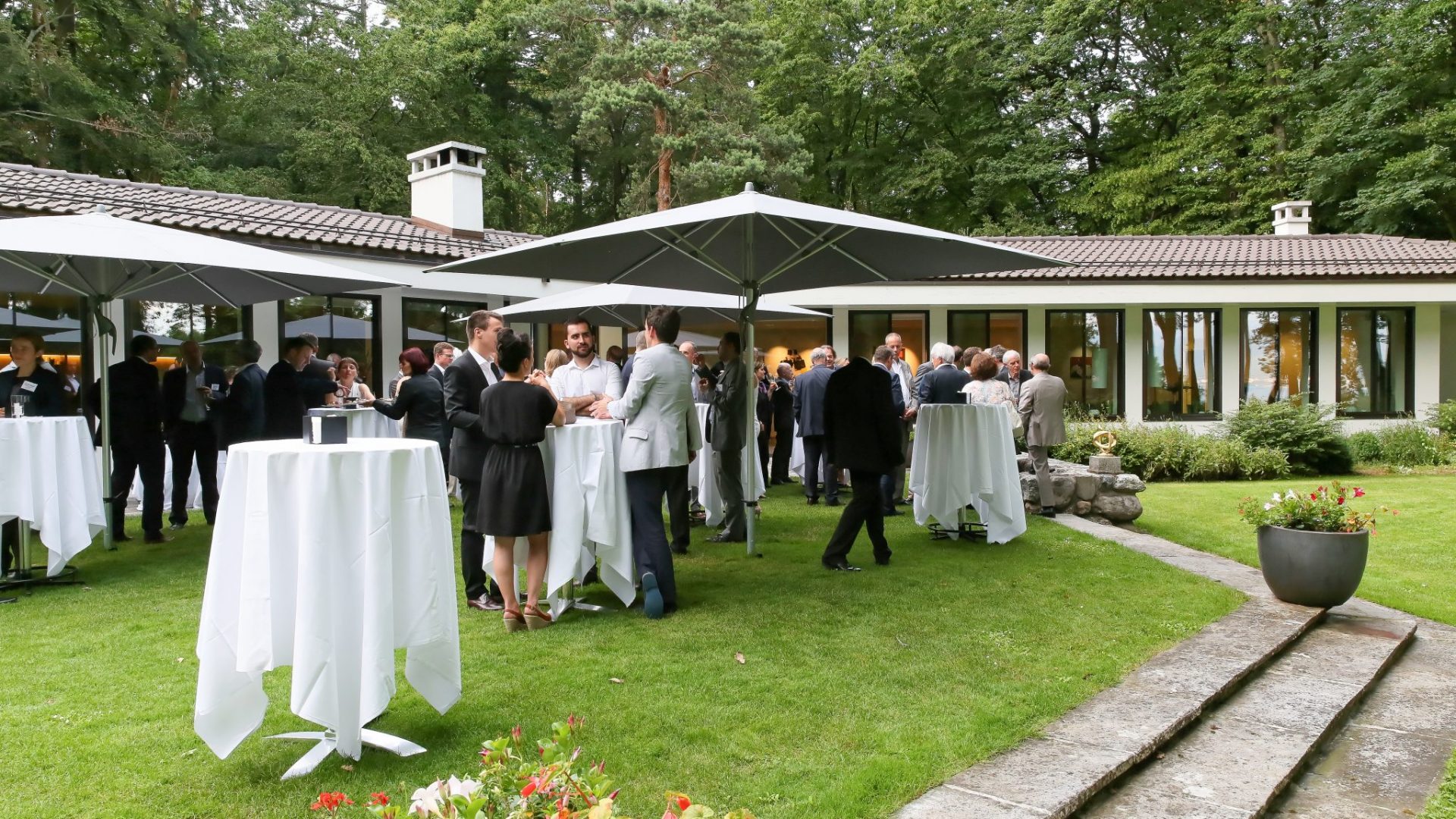 Des Alumni discutant autour d'une table, à l'extérieur d'un bâtiment, durant la Garden Party organisée en 2016.