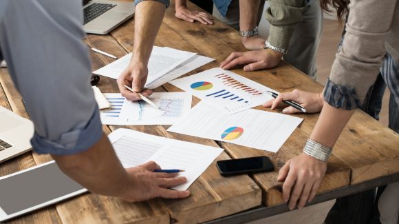 Businessman,And,Woman,Discussing,On,Stockmarket,Charts,In,Office