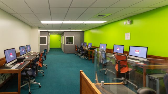 Digital Media Lab with bright green walls, a service desk, Mac desktop computers, scanners, and Music Booths in the background.