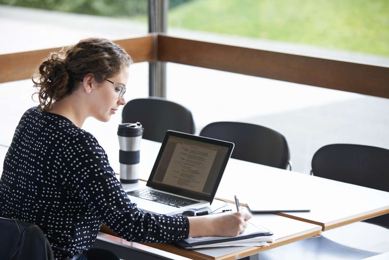 Woman working at table with notebook and laptop