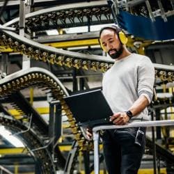 Man standing next to conveyor belts with laptop